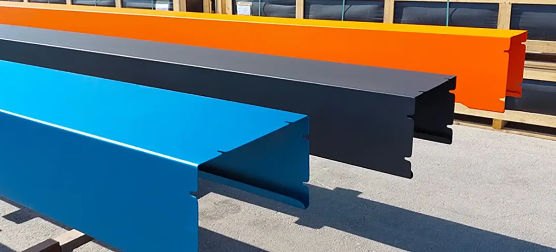 habillage Trois profilés métalliques de couleurs bleu, noir et orange sont alignés horizontalement sur un sol en béton.