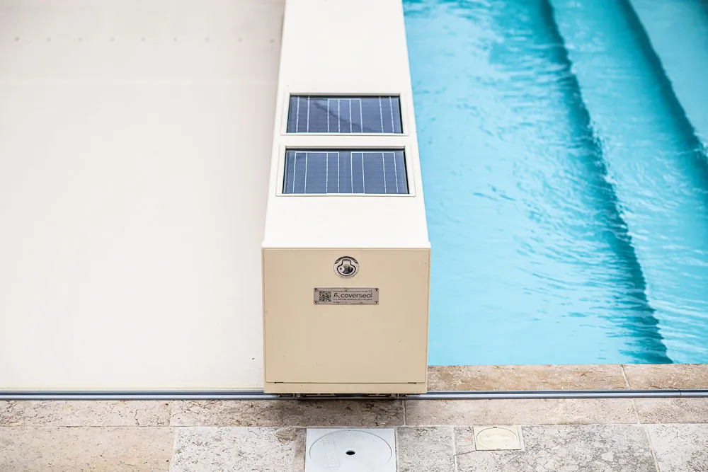 Un dispositif beige avec des panneaux solaires est installé au bord d'une piscine bleue, entourée de carrelage clair.