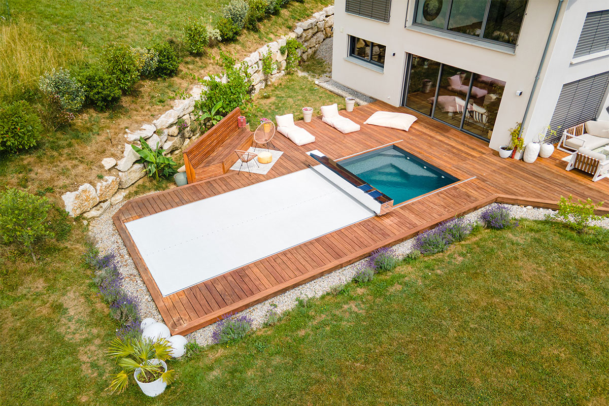 BlackPuppy Piscine moderne avec terrasse en bois et couverture automatique fermée, intégrée dans un jardin paysager.